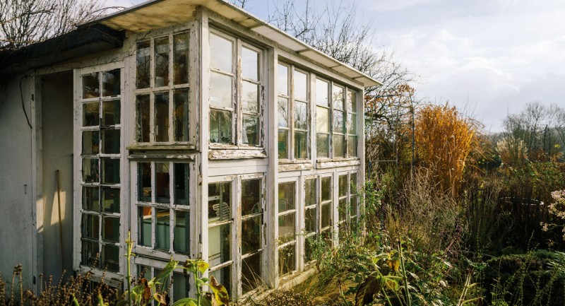 Ein Gewächshaus, gebaut aus alten Fenstern, steht im grünen Garten im Frühjahr