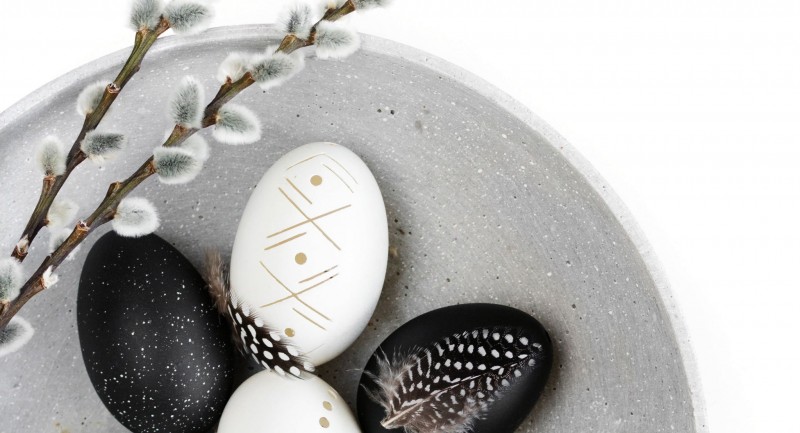 Eine graue Schale mit Ostereiern. Einige Eier sind schwarz gefärbt und haben weiße Muster; andere sind weiß und mit feinen Mustern bemalt.