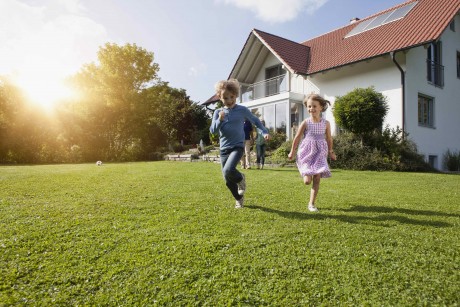 Zwei Kinder laufen über den Rasen und im Hintergrund ist ein neues Haus zu sehen.