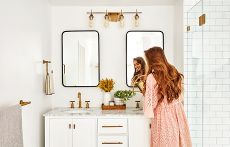 Frau steht im Bad vor den Waschbeckenschrank mit Spiegel. 