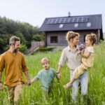 Eine Familie spaziert auf einer grünen Wiese vor ihrem Eigenheim.
