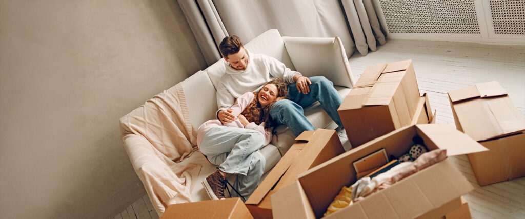 Ein junges Paar liegt auf dem Sofa in einer neuen Wohnung umgeben von Umzugskartons.