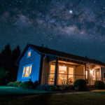 Eine Nachtaufnahme eines Einfamilienhauses in ländlicher Gegend über dem die Milchstraße am Himmel sichtbar ist.