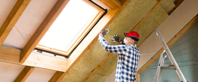 Mann baut im Dachboden Wärmedämmung ein.