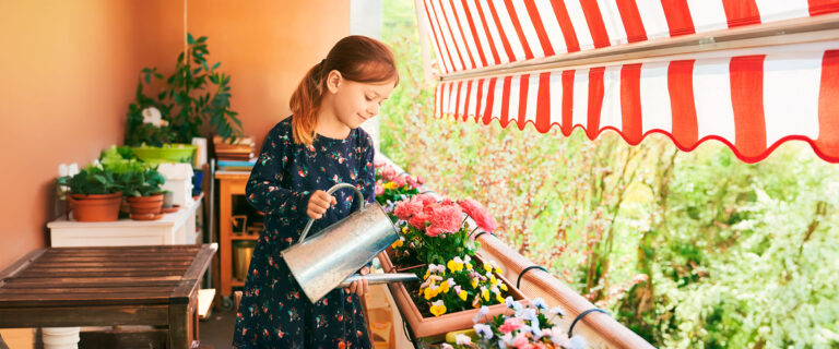 Ein junges Mädchen steht auf dem Balkon und gießt Blumen.