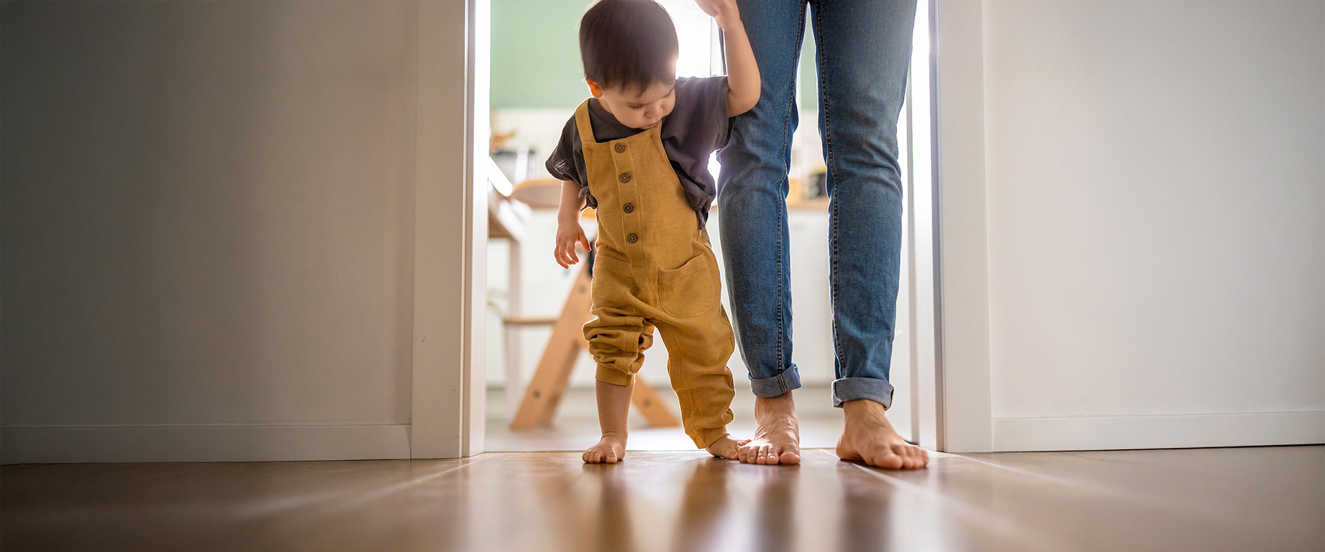 Kleinkind läuft an der Hand der Mutter auf einem Fußboden.