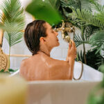 Frau sitzt in der Badewanne umgeben von Pflanzen.