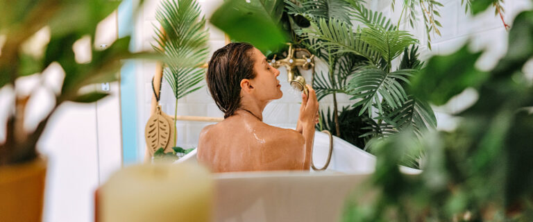 Frau sitzt in der Badewanne umgeben von Pflanzen.